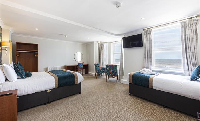 Image shows a triple room, with a double bed on the left and a single bed on the right. Two windows show the view out over the Irish Sea.